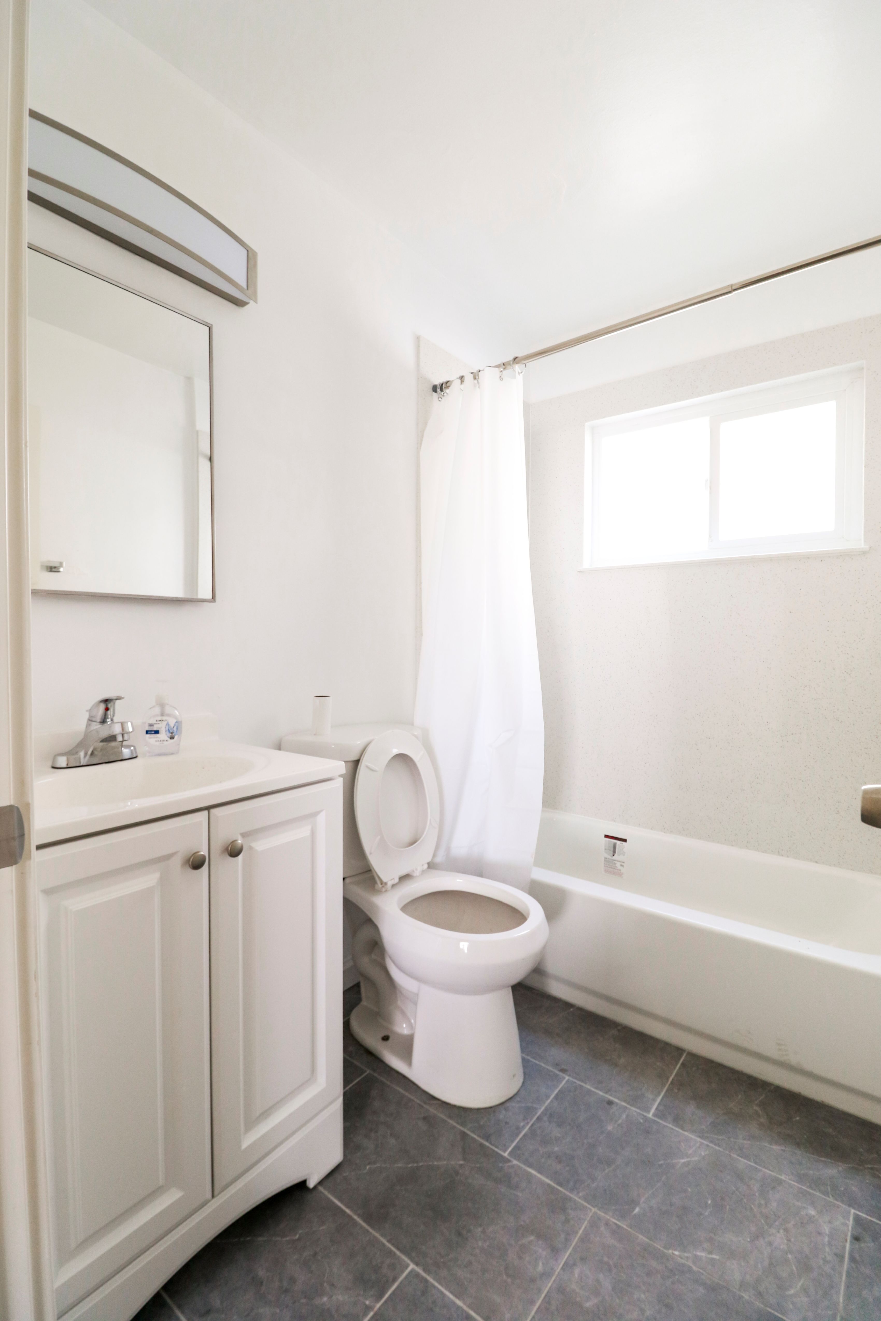 A white toilet is in a bathroom with a white cabinet and a window.
